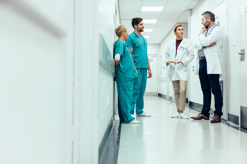 Group,Of,Medical,Staff,Discussing,In,Clinic,Hallway.,Healthcare,Professionals